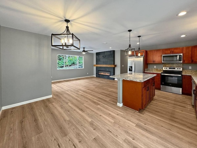 kitchen with stainless steel appliances, a center island, light stone counters, a fireplace, and decorative light fixtures