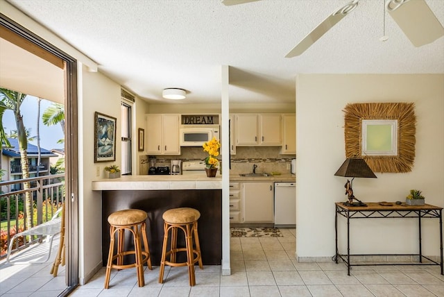 kitchen with sink, a breakfast bar area, tasteful backsplash, light tile patterned floors, and white appliances