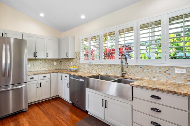 kitchen featuring sink, appliances with stainless steel finishes, light stone countertops, white cabinets, and vaulted ceiling