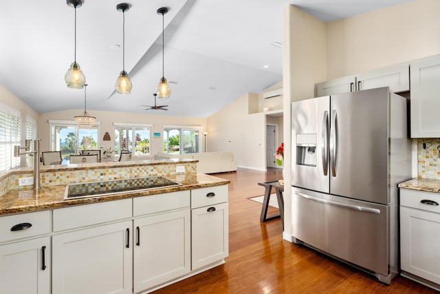 kitchen featuring pendant lighting, black electric stovetop, stainless steel fridge, and white cabinets