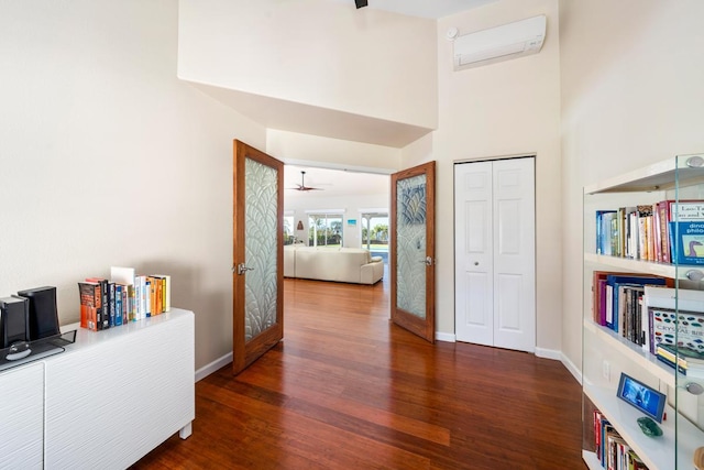 hallway with a wall mounted air conditioner, dark hardwood / wood-style floors, french doors, and a towering ceiling