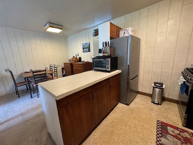 kitchen featuring dark brown cabinetry, black gas stove, stainless steel refrigerator, and kitchen peninsula