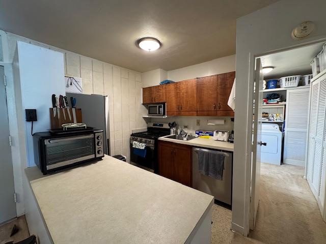 kitchen with washer / clothes dryer, appliances with stainless steel finishes, and light colored carpet