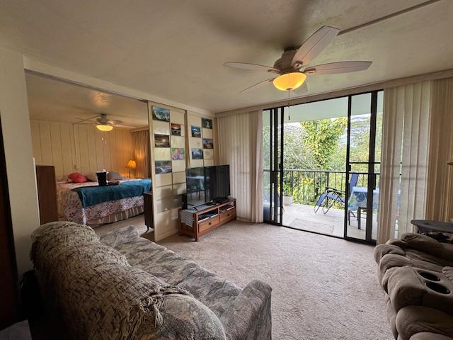 living room with ceiling fan, a wall of windows, wooden walls, and carpet