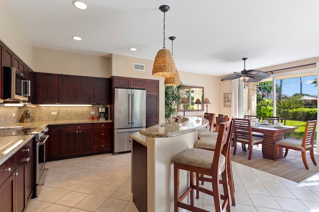 kitchen with a kitchen bar, tasteful backsplash, light tile patterned floors, appliances with stainless steel finishes, and pendant lighting