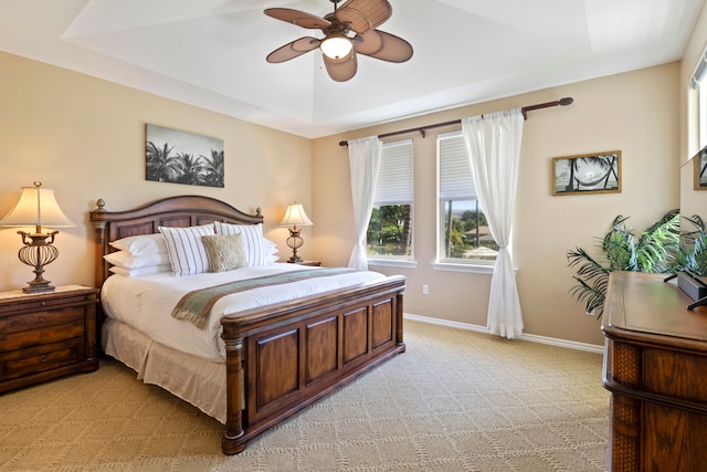 bedroom with ceiling fan, light colored carpet, and a raised ceiling