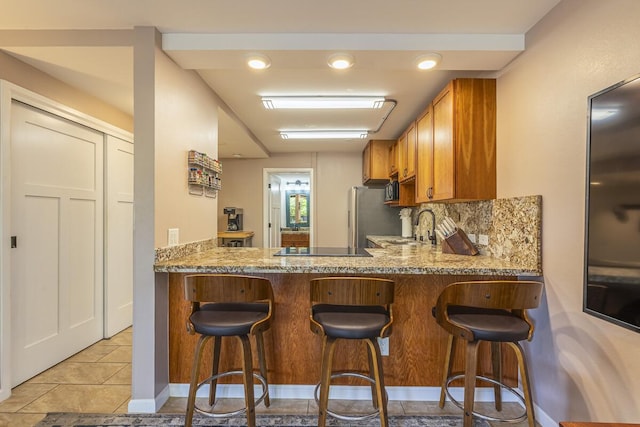 kitchen featuring sink, light tile patterned floors, kitchen peninsula, decorative backsplash, and black appliances