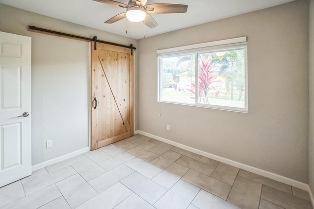 unfurnished bedroom with a barn door, baseboards, a ceiling fan, and light tile patterned flooring