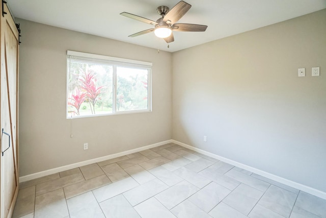 empty room with light tile patterned floors, a barn door, baseboards, and a ceiling fan