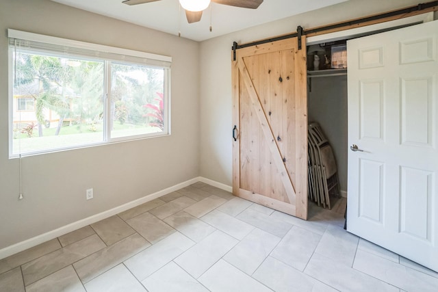 unfurnished bedroom with ceiling fan, a barn door, light tile patterned flooring, baseboards, and a closet