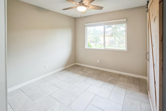 empty room with ceiling fan, a barn door, light tile patterned flooring, and baseboards