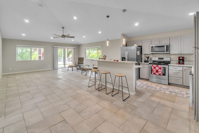 kitchen featuring stainless steel appliances, gray cabinets, a kitchen island, and light stone countertops