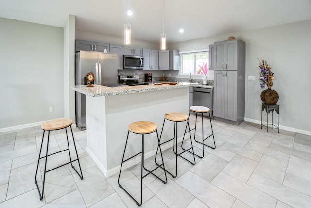 kitchen with a breakfast bar area, a center island, light stone countertops, gray cabinets, and stainless steel appliances