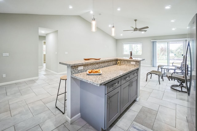 kitchen featuring a breakfast bar area, hanging light fixtures, freestanding refrigerator, an island with sink, and light stone countertops