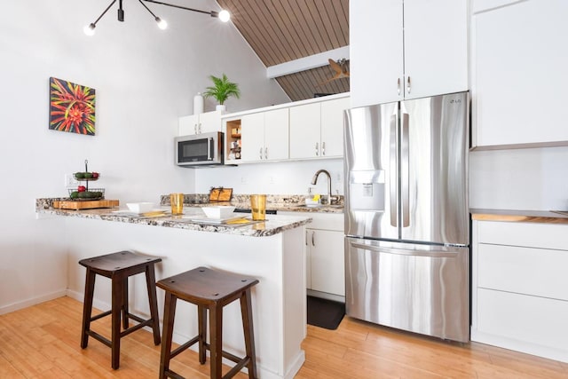 kitchen featuring sink, white cabinetry, a kitchen breakfast bar, stainless steel appliances, and light stone countertops