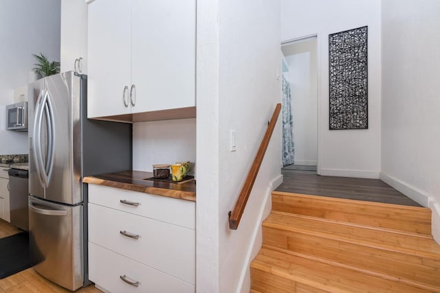 kitchen featuring wood-type flooring, appliances with stainless steel finishes, white cabinets, and wood counters