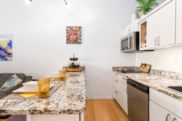 kitchen featuring appliances with stainless steel finishes, white cabinets, light stone counters, and light hardwood / wood-style flooring