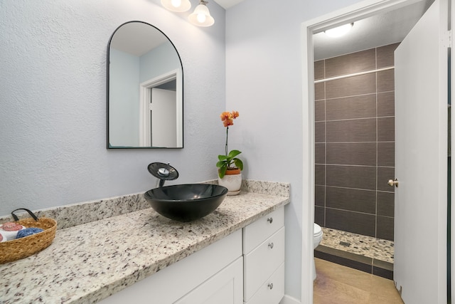 bathroom featuring tile patterned floors, toilet, tiled shower, and vanity