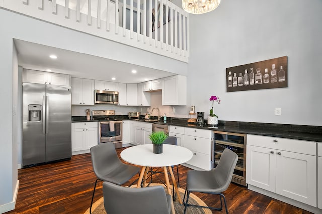 kitchen with beverage cooler, a high ceiling, dark wood-type flooring, appliances with stainless steel finishes, and dark countertops