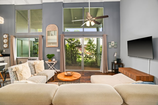 living room featuring a ceiling fan, wood finished floors, baseboards, and a towering ceiling