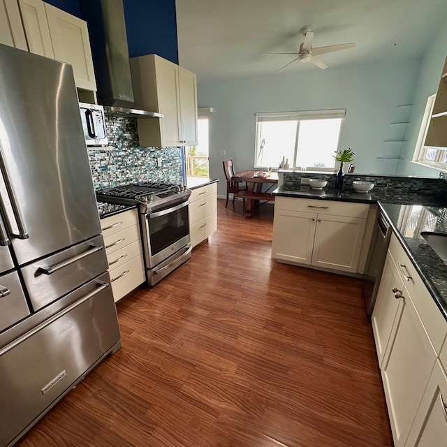 kitchen featuring white cabinetry, appliances with stainless steel finishes, dark stone countertops, and wall chimney range hood