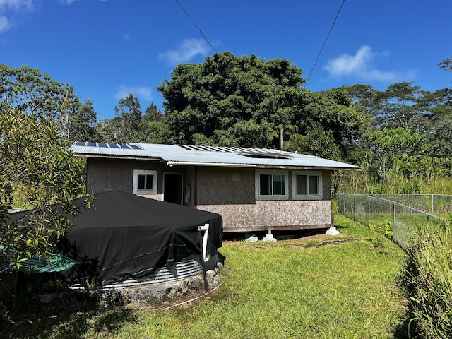 rear view of property featuring a yard and solar panels