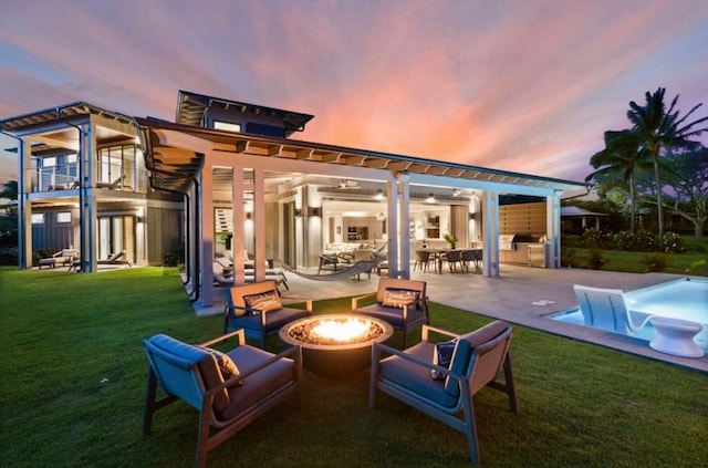 back house at dusk with a pergola, a yard, a patio area, and a fire pit