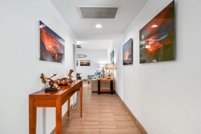 hall featuring light wood finished floors, visible vents, and baseboards