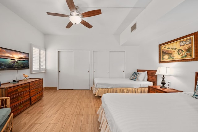 bedroom featuring light wood-style floors, visible vents, ceiling fan, and two closets