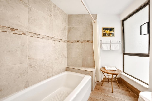 bathroom featuring toilet, baseboards,  shower combination, and wood finished floors