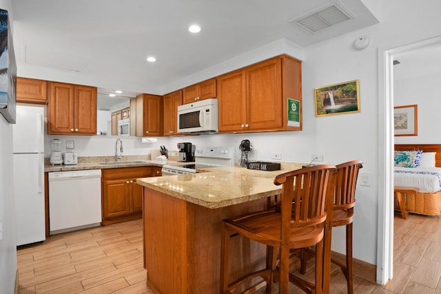 kitchen featuring white appliances, visible vents, brown cabinets, a peninsula, and a sink