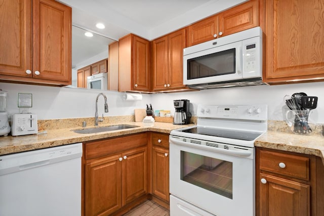 kitchen with light stone counters, white appliances, brown cabinetry, and a sink