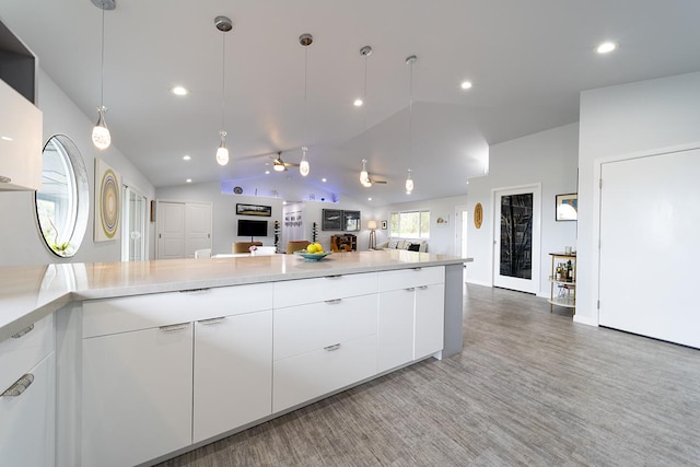 kitchen with pendant lighting, light countertops, open floor plan, white cabinetry, and vaulted ceiling