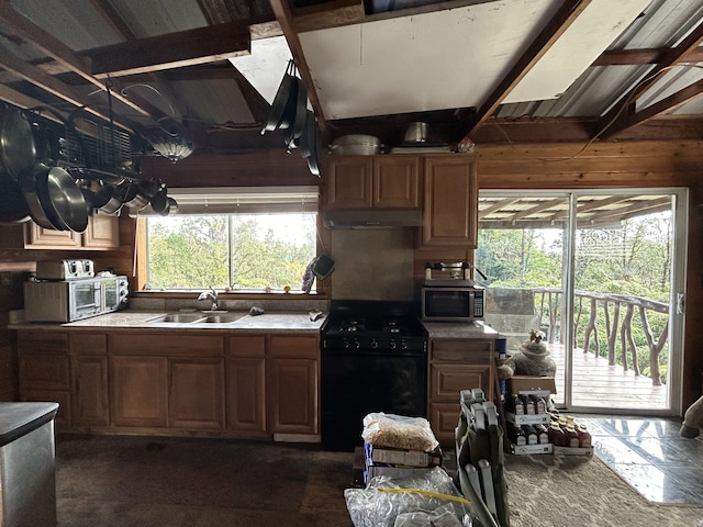 kitchen featuring wooden walls, sink, gas stove, and beam ceiling