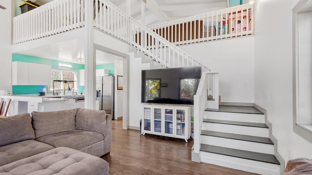 living room featuring baseboards, a towering ceiling, dark wood-style floors, stairway, and beamed ceiling