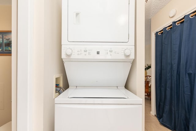 laundry area featuring light tile patterned flooring, stacked washer / dryer, and a textured ceiling