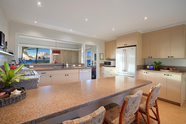 kitchen with pendant lighting, a breakfast bar area, kitchen peninsula, cream cabinets, and white appliances