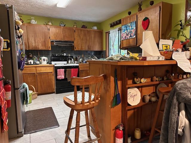 kitchen featuring ventilation hood, stainless steel fridge, backsplash, a textured ceiling, and black / electric stove