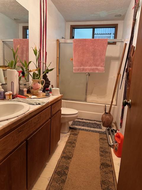 full bathroom featuring vanity, toilet, a textured ceiling, and bath / shower combo with glass door