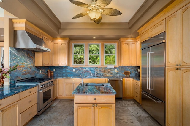 kitchen featuring premium appliances, decorative backsplash, light brown cabinetry, a sink, and dark stone countertops