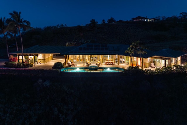 back of house at twilight with a patio area and a pool with connected hot tub