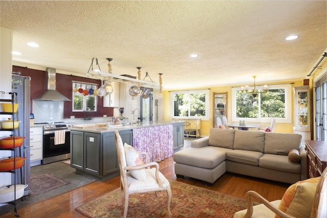 kitchen featuring stainless steel electric stove, pendant lighting, a kitchen island with sink, dark wood-type flooring, and wall chimney exhaust hood