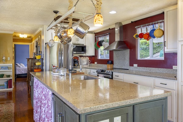 kitchen with wall chimney exhaust hood, sink, white cabinetry, a center island with sink, and appliances with stainless steel finishes