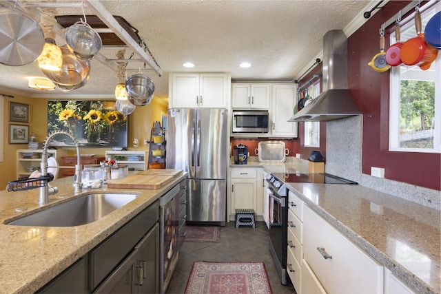 kitchen with sink, stainless steel appliances, light stone countertops, white cabinets, and wall chimney exhaust hood