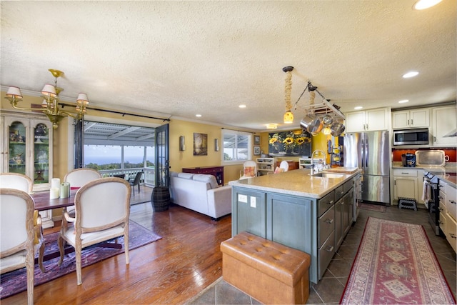 kitchen featuring sink, hanging light fixtures, a kitchen island with sink, stainless steel appliances, and light stone countertops