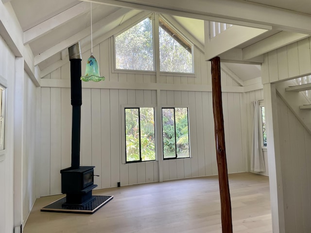 unfurnished living room featuring lofted ceiling with beams, wood finished floors, a wood stove, and a healthy amount of sunlight