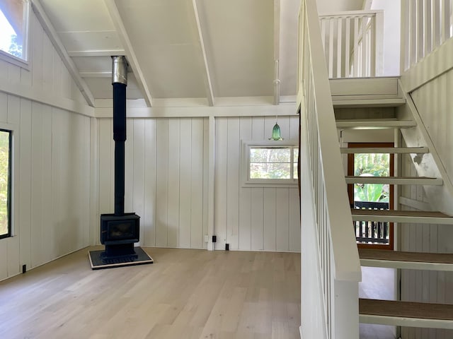 unfurnished living room with beam ceiling, wood finished floors, and a wood stove