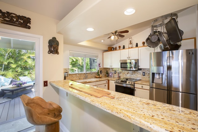 kitchen with white cabinets, a kitchen bar, kitchen peninsula, stainless steel appliances, and light stone countertops