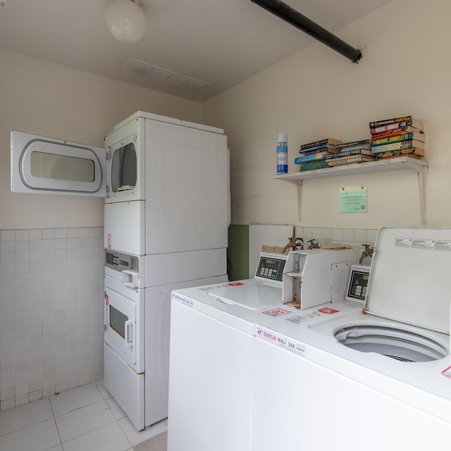 laundry area with tile walls, stacked washer and dryer, light tile patterned floors, and washing machine and clothes dryer