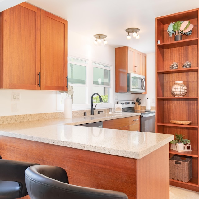 kitchen featuring light stone counters, sink, stainless steel appliances, and kitchen peninsula